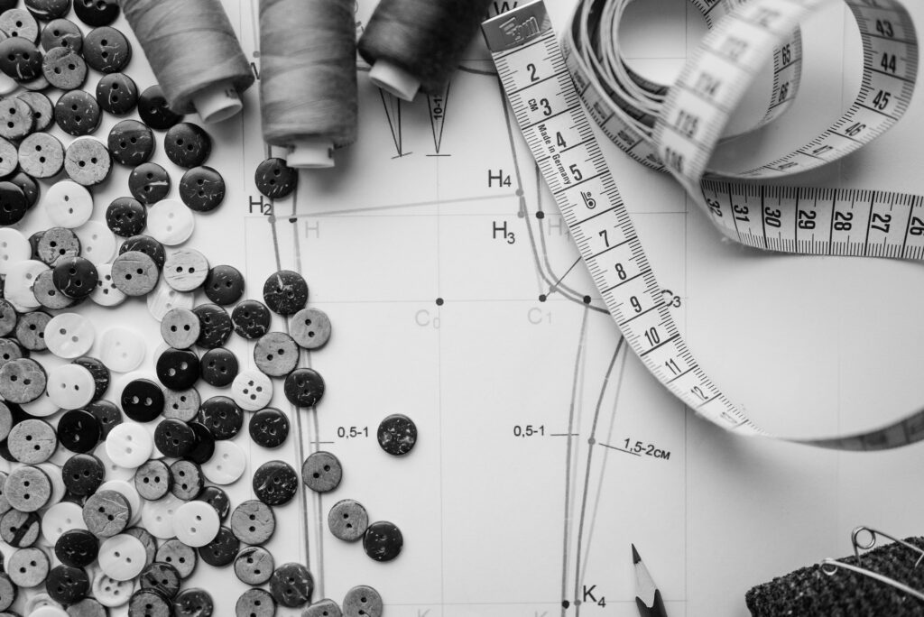 Black and white sewing essentials flatlay with buttons, tape, and patterns.